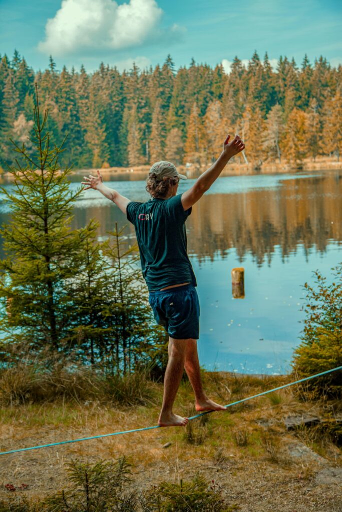 Man skillfully balances on a slackline by a serene lake, surrounded by nature in Bayreuth, Germany.